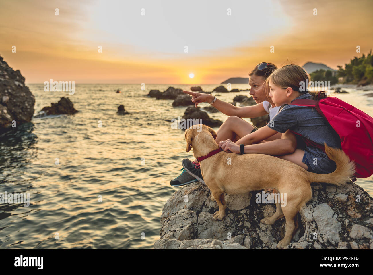 Mère et fille avec un petit chien jaune de la randonnée le long de la plage pendant le coucher du soleil Banque D'Images