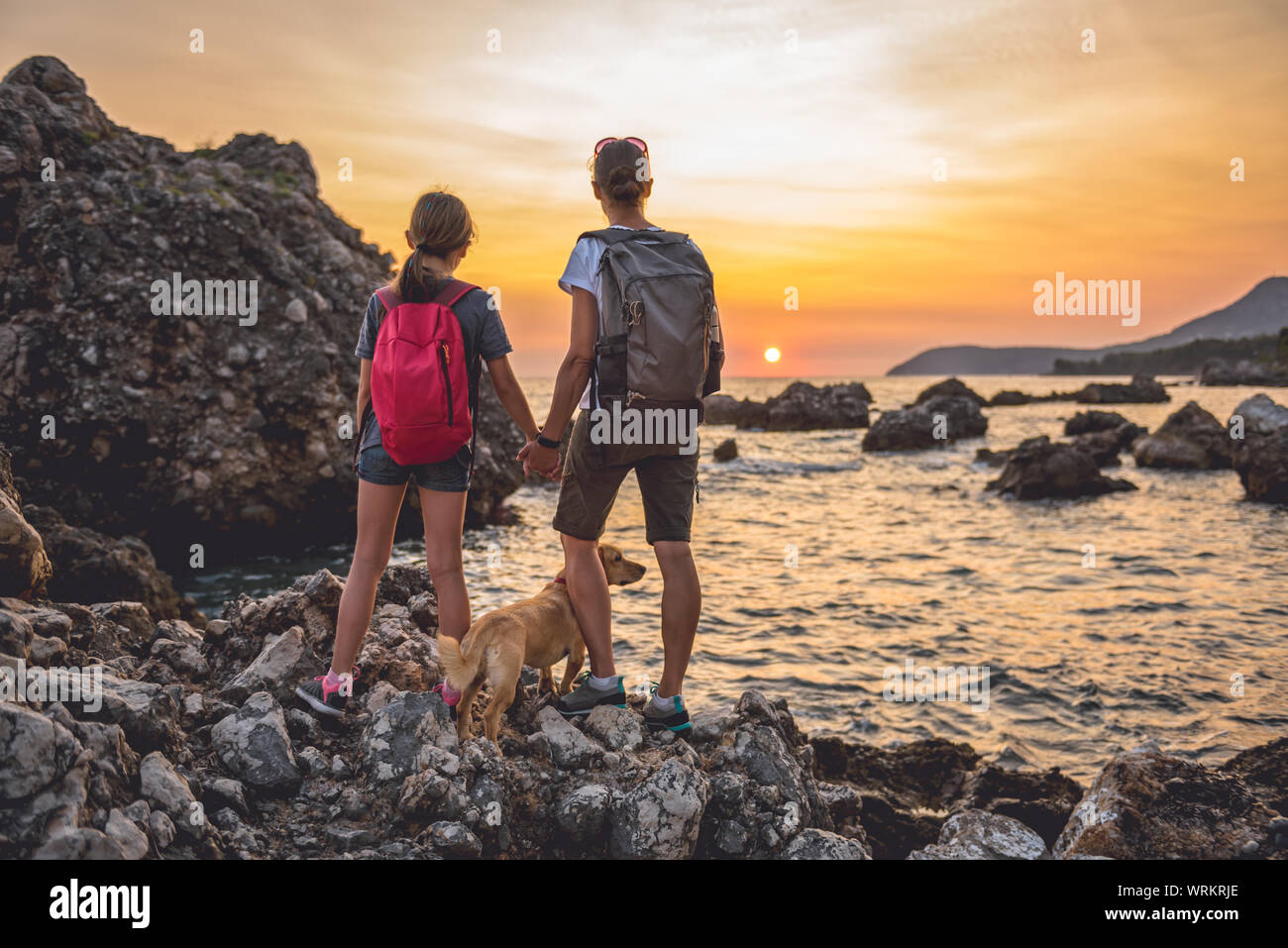 Mère et fille avec un petit chien jaune de la randonnée le long de la plage pendant le coucher du soleil Banque D'Images Mère et fille avec un petit chien jaune de la randonnée le long de la plage pendant le coucher du soleil Banque D'Images