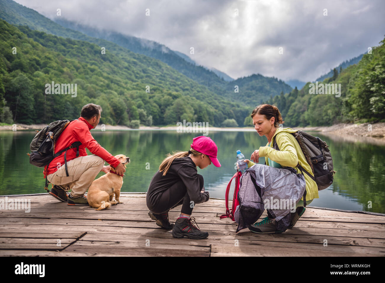 Famille avec le petit chien jaune reposant sur une jetée par le lac et montagnes brumeux Banque D'Images