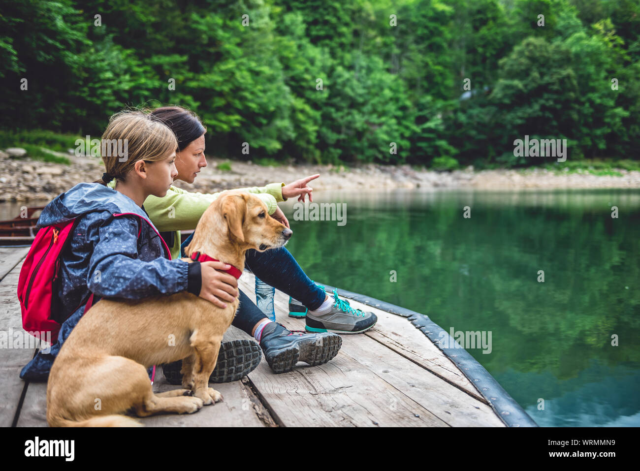 Mère et fille avec un petit chien jaune reposant sur un quai et à la recherche à Mountain Lake Banque D'Images
