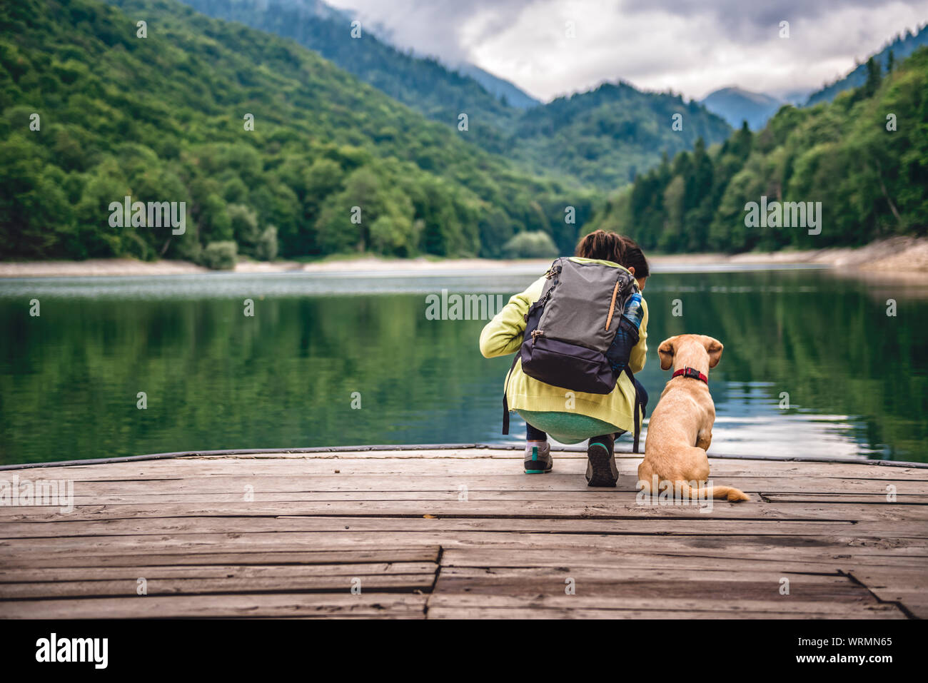 Femme avec un petit chien jaune sur la jetée par le lac de montagne Banque D'Images