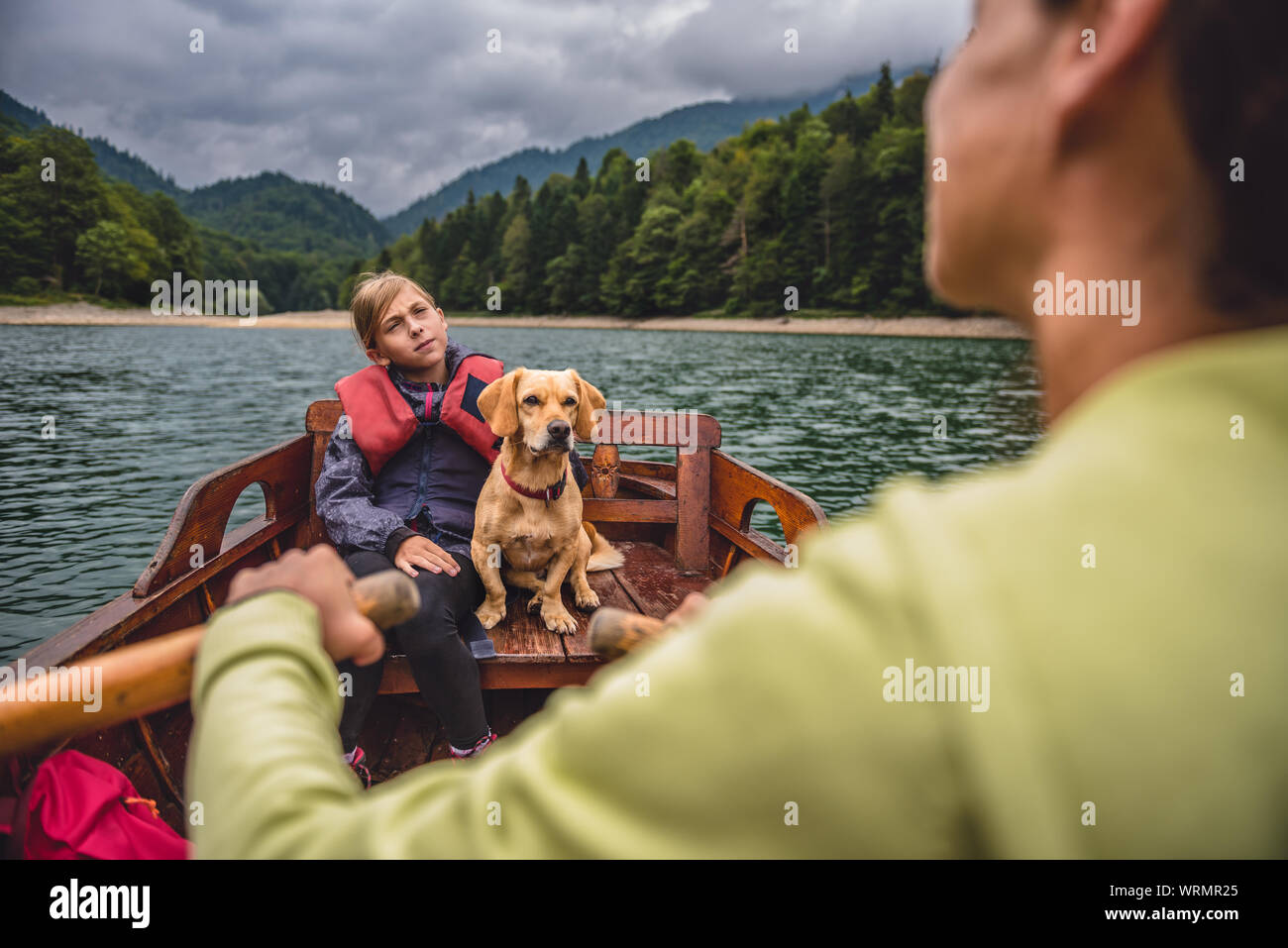 Mère et fille avec un petit chien jaune un bateau d'aviron sur un lac de montagne Banque D'Images
