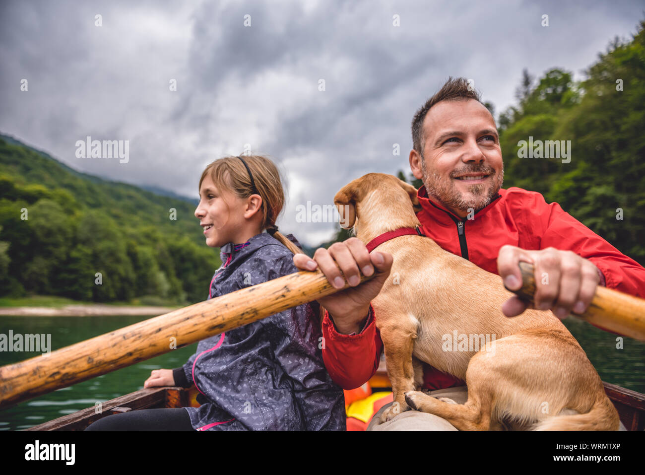 Père et fille avec un petit chien jaune un bateau d'aviron sur un lac de montagne Banque D'Images