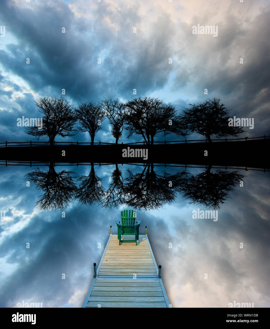 Image miroir de cinq arbres le long d'une route silhouetté contre nuages orageux avec une chaise Adirondack assis sur un quai, Stowe au Vermont, USA Banque D'Images