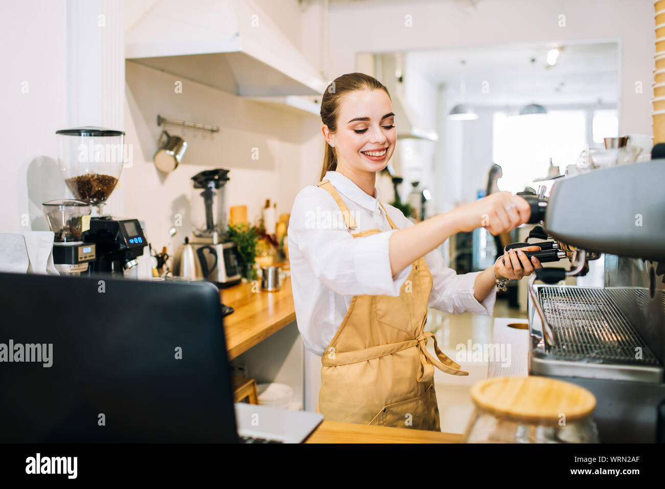 Jolie femme heureuse barista au comptoir bar, prépare à verser du café dans un café ou un restaurant moderne. Banque D'Images