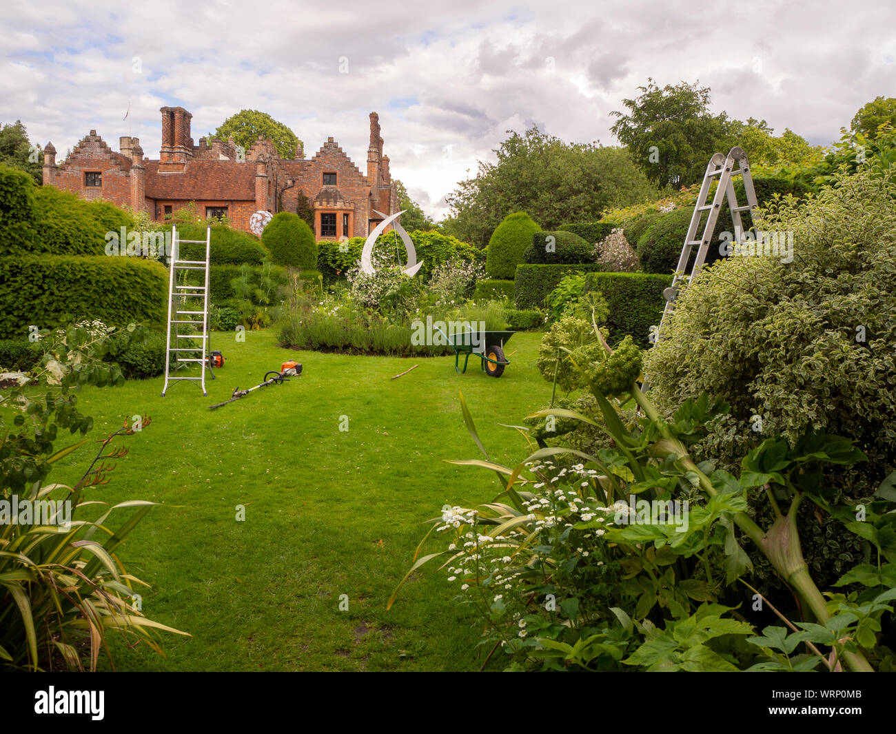 Chenies Manor avec jardin topiaire en cours d'entretien de jardin.Taille-haie, une brouette et les échelles sont en cours d'utilisation sur la pelouse. Banque D'Images