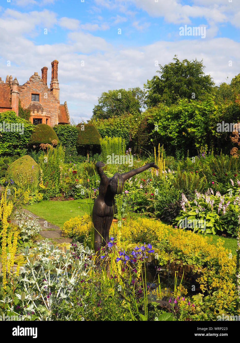 Portrait de Chenies manoir et jardin en contrebas, bassin d'agrément avec Alan Biggs' sculpture;f resh plante verte frontière en fin d'après-midi de juin. Banque D'Images