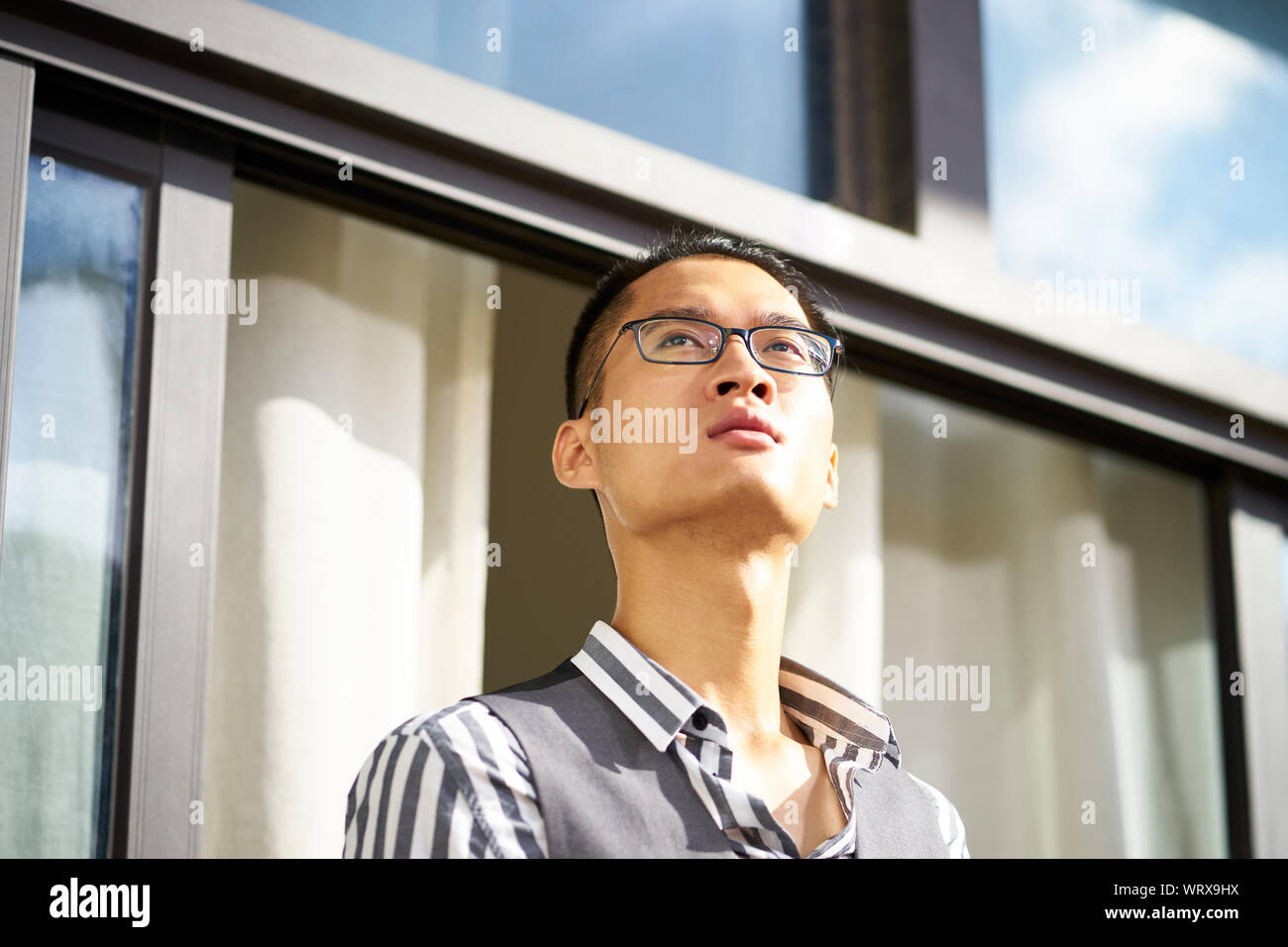 Young Asian man standing on patio looking at view Banque D'Images