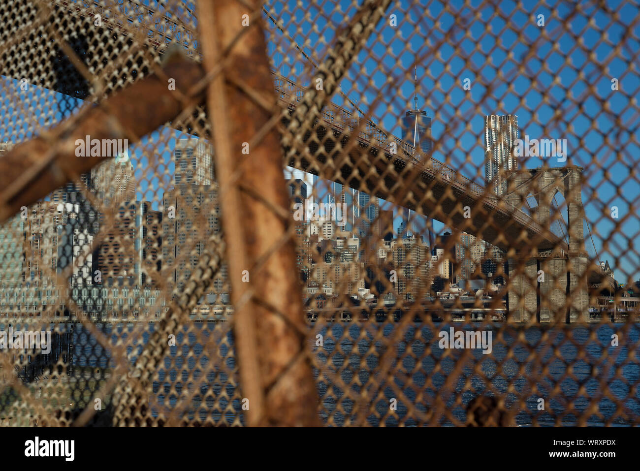 Résumé regardez le Pont de Brooklyn à travers une clôture à mailles de chaîne rouillée au Brooklyn Bridge Park à New York. Banque D'Images