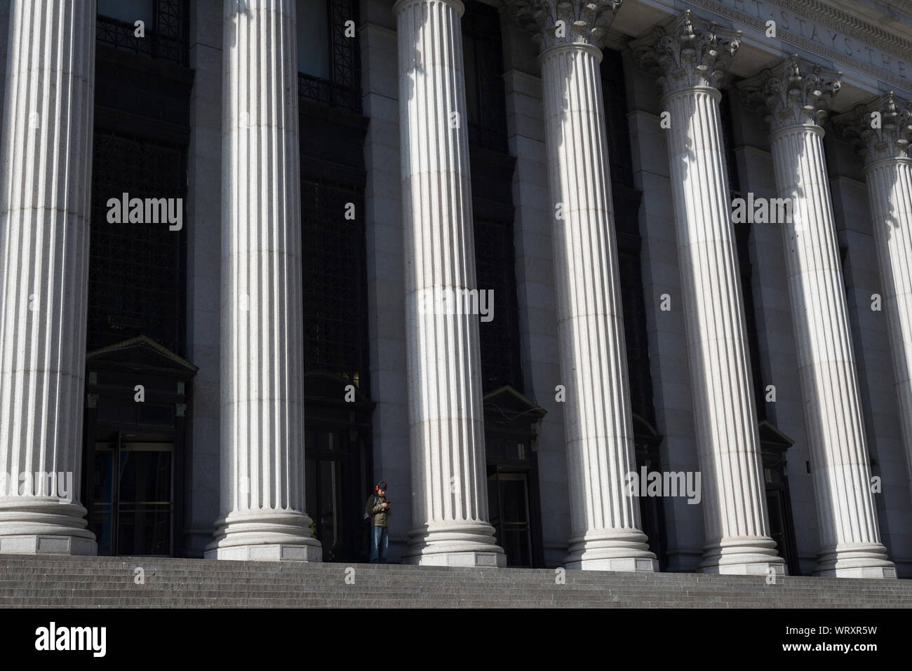 Un homme regardant son cell-phone sur les marches de l'United States Post Office James A. Farley building à Midtown Manhattan, New York. Banque D'Images