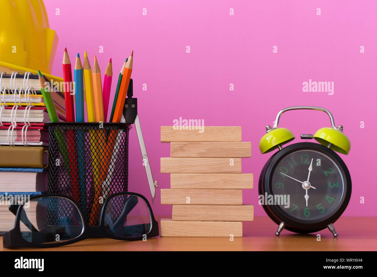 Empiler des blocs de bois avec des crayons, des diviseurs, lunettes, casque de construction, de l'horloge et pile de livre sur la table en bois, l'arrière-plan de sélection isolés en bois blanc Banque D'Images