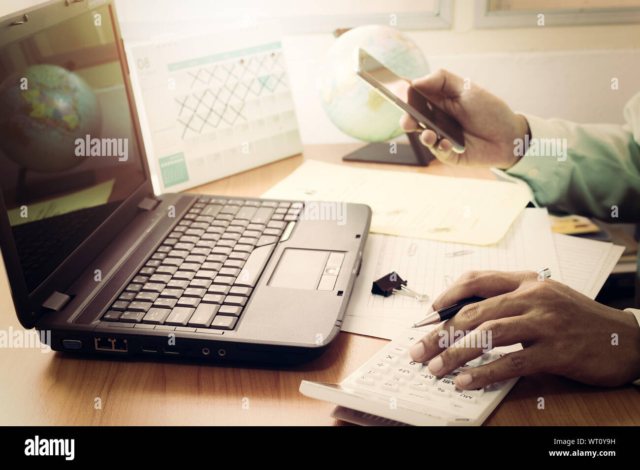 L'homme travaillant avec la calculatrice, business document, smart phone et l'ordinateur portable sur Office 24 dans vintage tone Banque D'Images