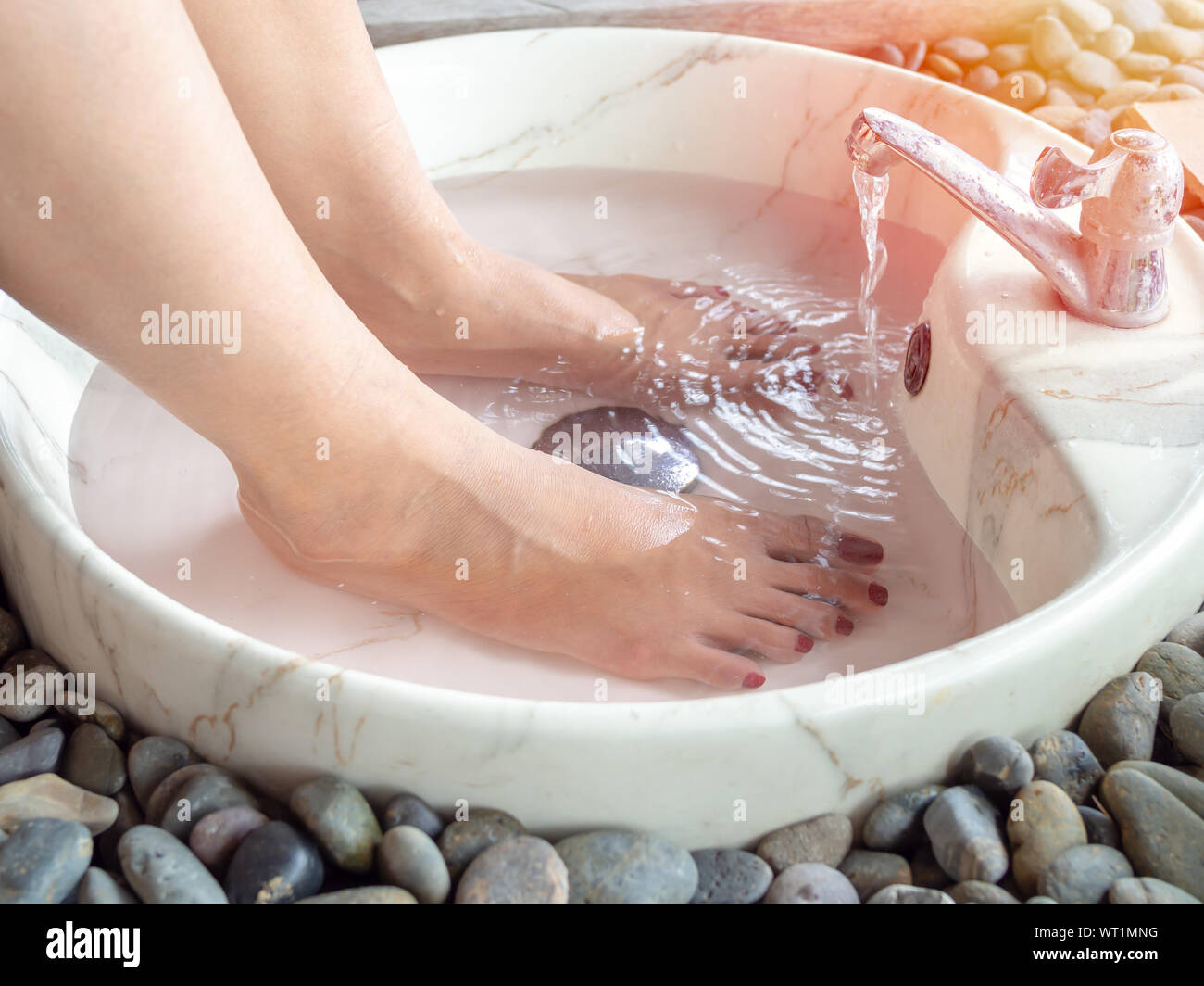 Les pieds dans un spa pour les pieds lavabo en marbre avec de l'eau découlant de robinet. Le sel d'Epsom pied soak concept. Banque D'Images