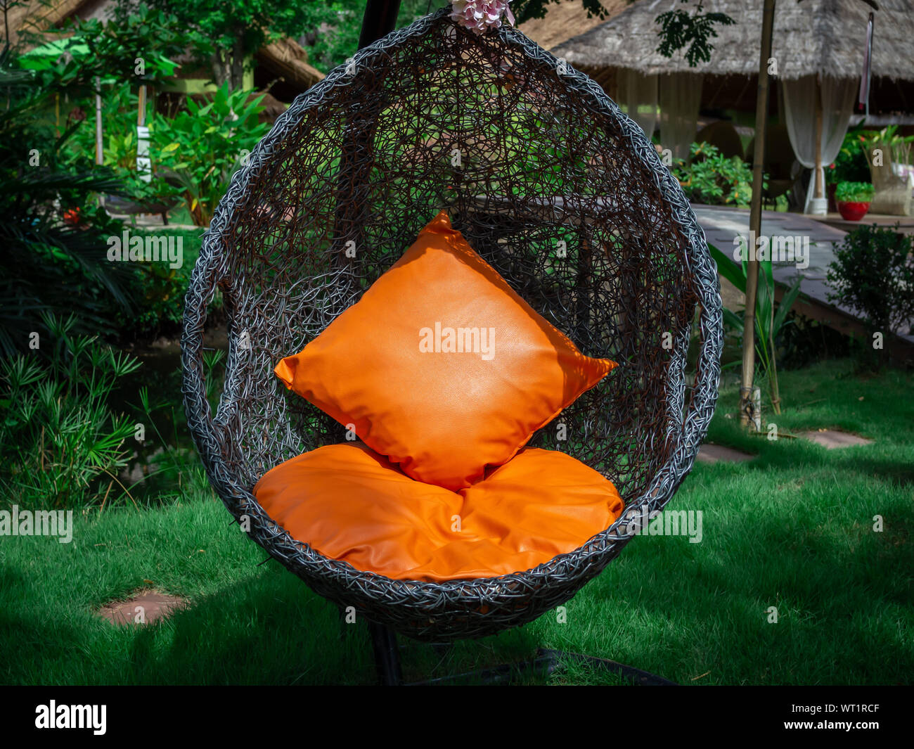 Chaise longue en rotin noir moderne oeuf suspendu chaise avec coussin  orange dans le jardin Photo Stock - Alamy