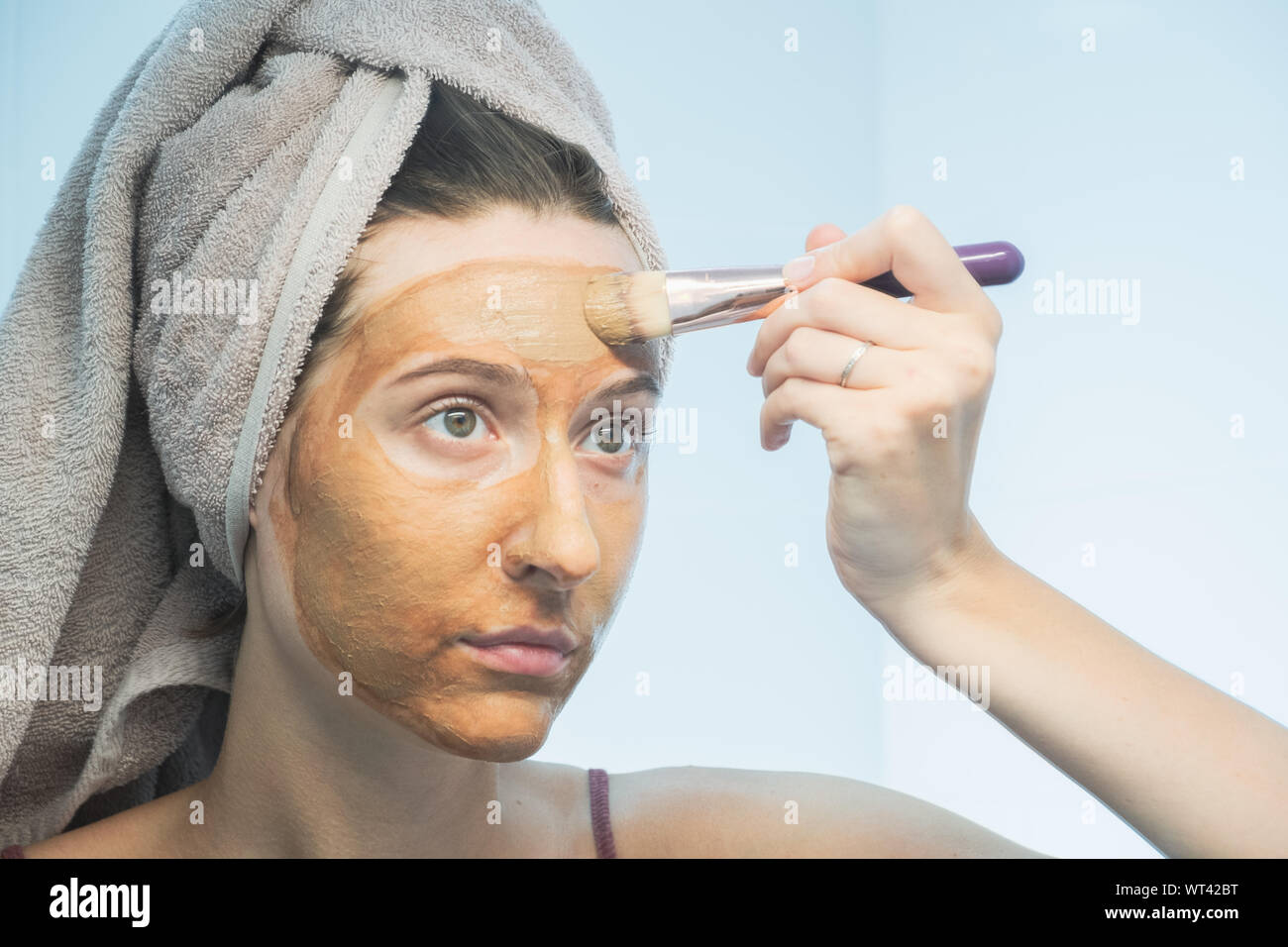 Une jeune femme met un masque d'argile sur le visage avec un pinceau dans une salle de bains privative. Le concept de l'autogestion, bon soins du visage, soins quotidiens de la peau Banque D'Images