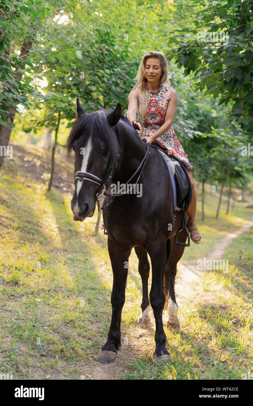 Jeune femme dans une robe colorée lumineuse équitation un cheval noir dans  le parc Photo Stock - Alamy