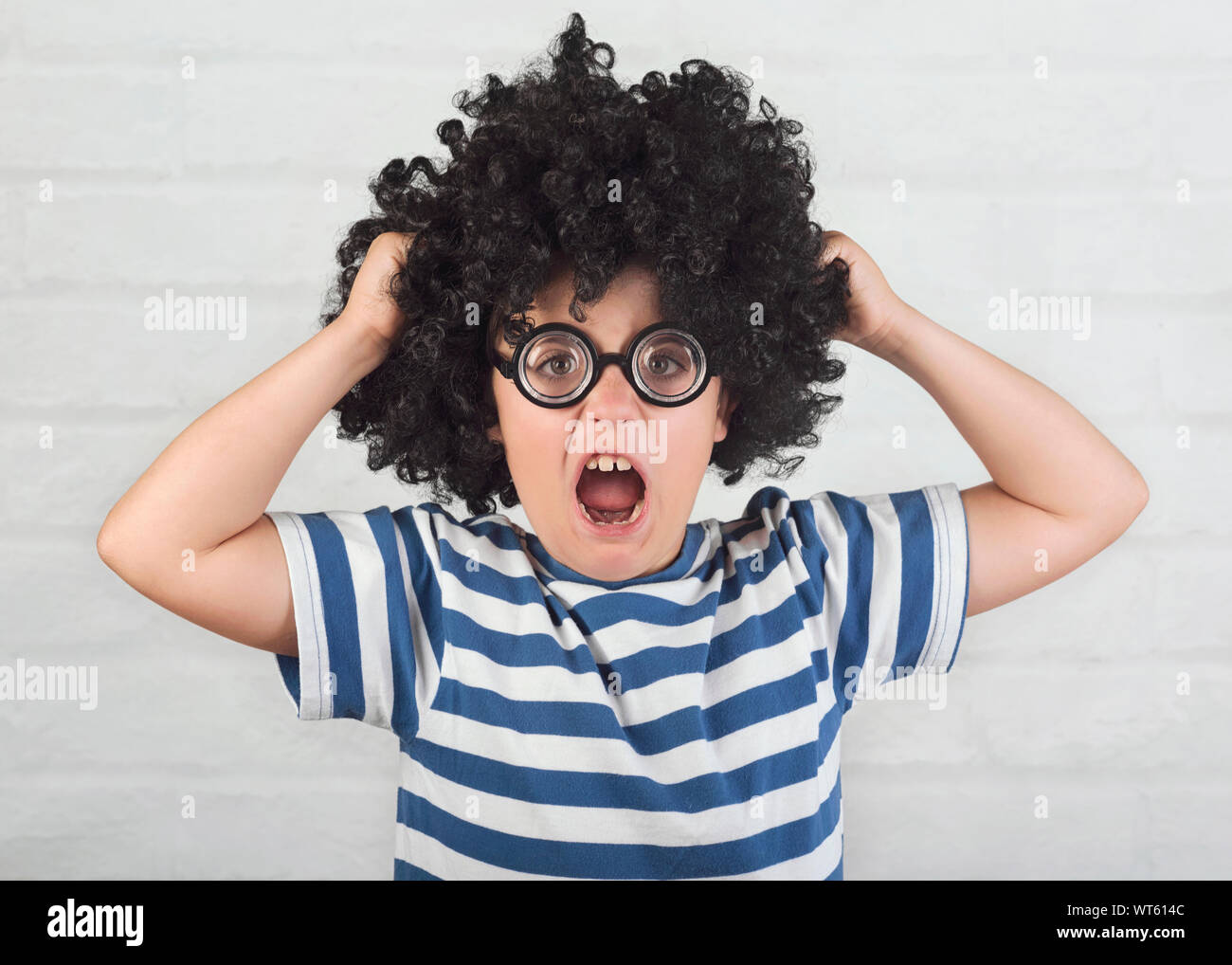 Angry boy wearing lunettes nerd qui tire ses cheveux sur fond brique Banque D'Images