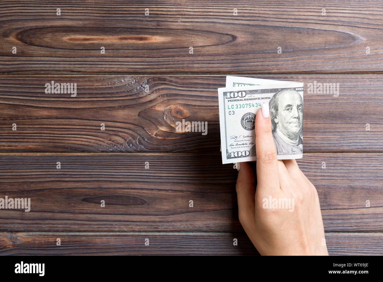 Un pack de 100 dollar bills in main féminine sur fond de bois. Concept de salaire avec l'exemplaire de l'espace. Banque D'Images