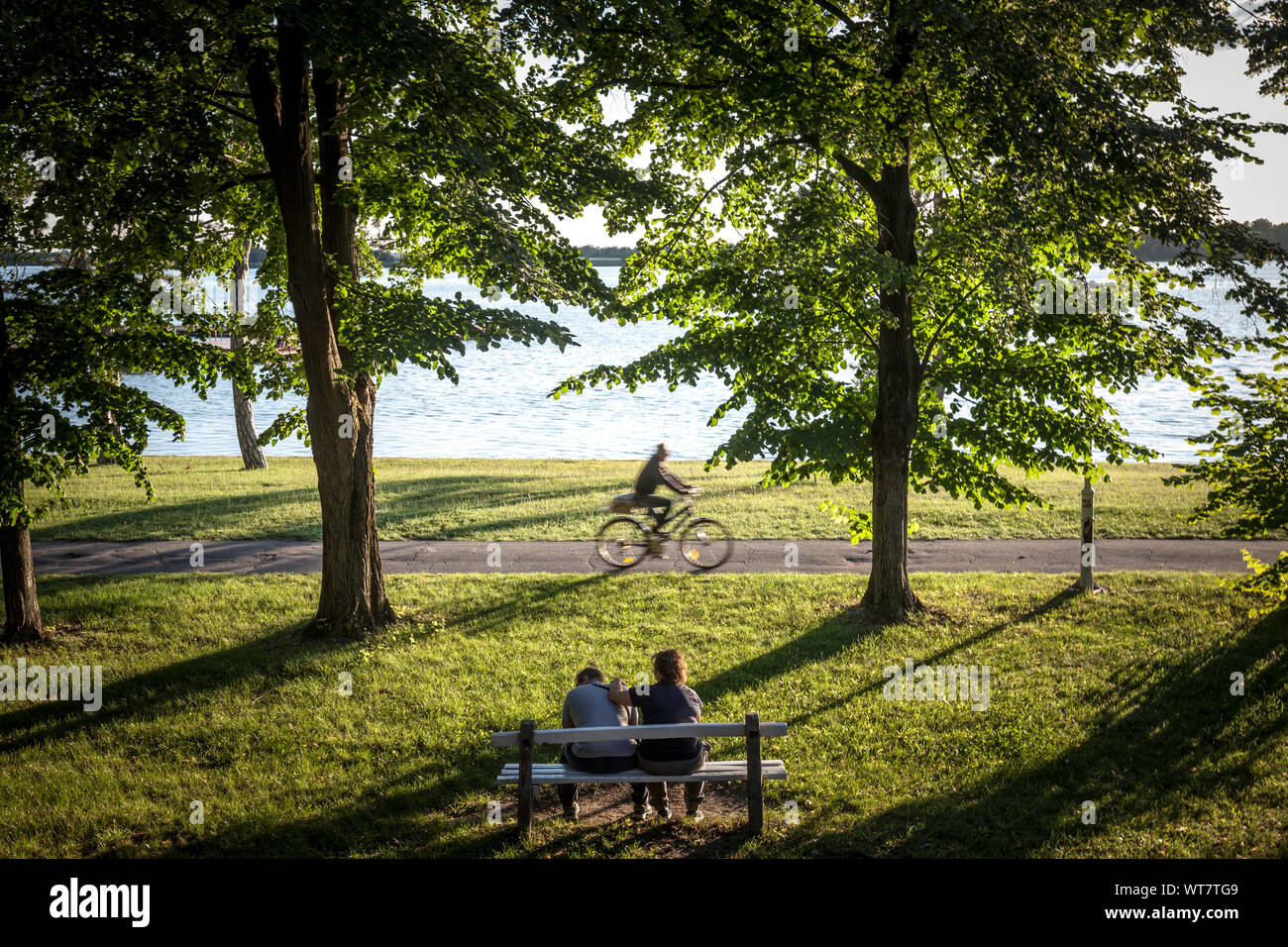 La Palice, SERBIE - 1 juillet 2018 : cycliste passant par sur la côte du lac Palic avec des gens assis sur un banc de Subotica, Serbie, avec une pelouse verte en Banque D'Images