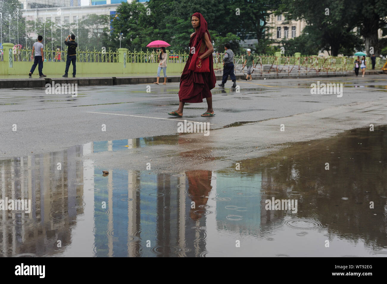 27.09.2013, Yangon, Myanmar, en Asie - un moine bouddhiste promenades par une flaque d'eau reflétant les bâtiments pendant la saison des pluies. Banque D'Images