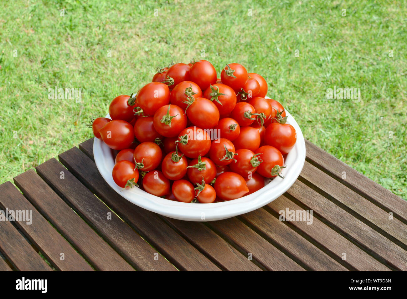 Gros tas de frais juteux Alerte Rouge les tomates cerise dans un plat de service en céramique blanche sur une table de jardin en bois Banque D'Images