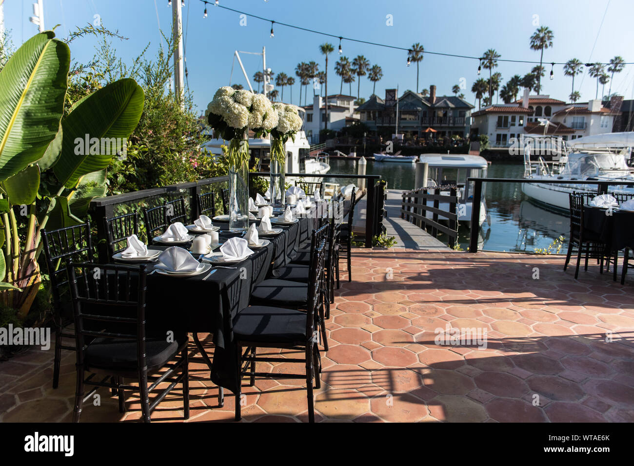 Serviettes pliées proprement en préparation pour grand groupe organisé le dîner sur une terrasse et donnant sur quai des bateaux du canal. Banque D'Images