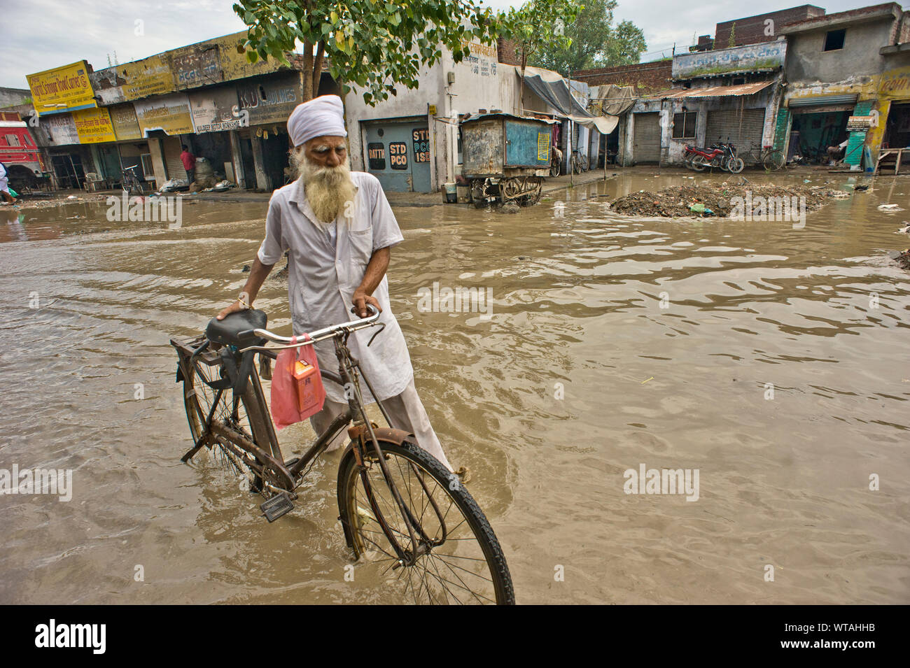 Homme sikh portant son vélo dans les rues d'un jour d'inondation Banque D'Images
