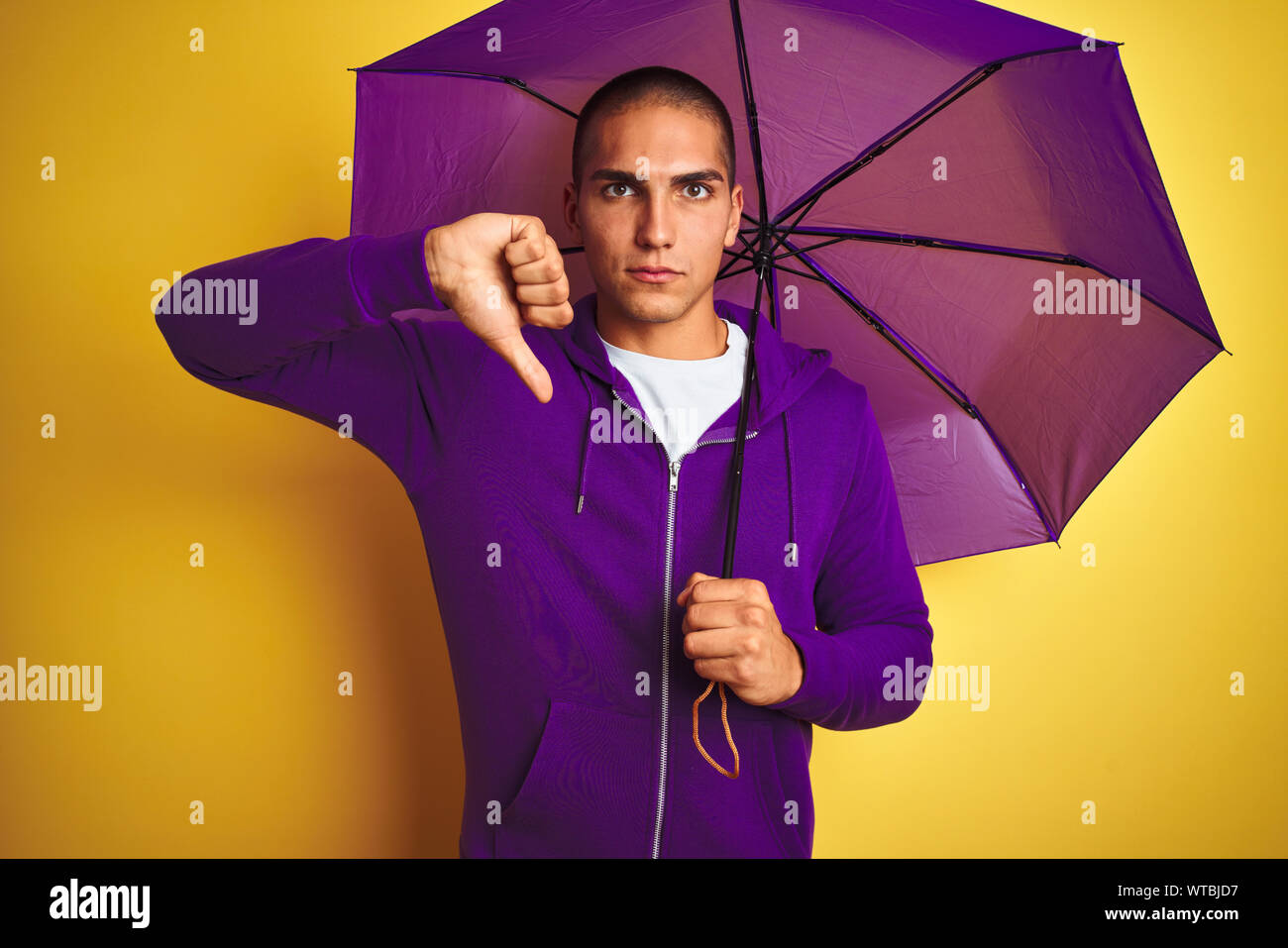 Beau jeune homme portant un parapluie violet sur jaune fond isolé, visage  en colère avec signe négatif montrant non avec vers le bas, le rejet Photo  Stock - Alamy