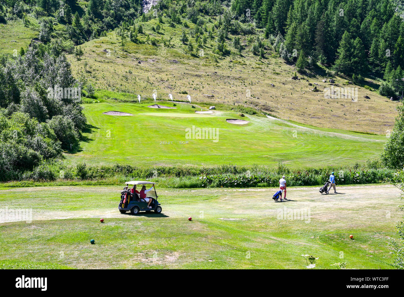 Vue panoramique sur un parcours de golf de montagne avec les personnes d'âge moyen sur un chariot de golf et de transporter des sacs de golf, Val Ferret, Courmayeur, vallée d'Aoste, Alpes, Italie Banque D'Images