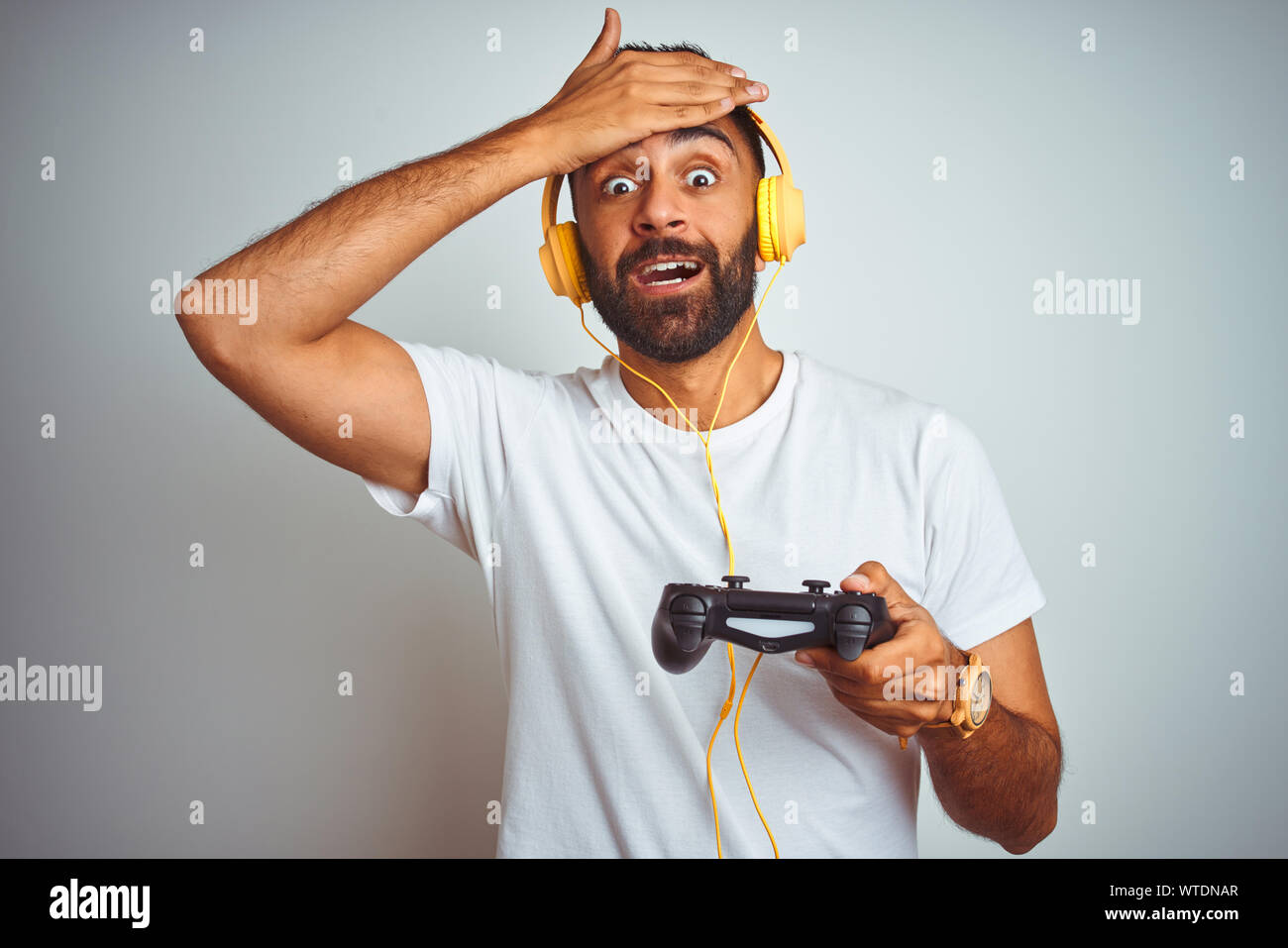 Les indiens arabes gamer man playing video game de l'utilisation des écouteurs sur fond blanc isolé a souligné avec la main sur la tête, choqué par la honte et la surprise f Banque D'Images