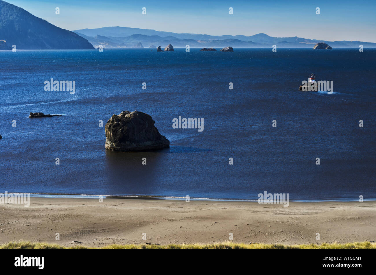 Plage et Mer falaises ci-dessous des piles à Port Orford, Oregon, avec un bateau traversant la baie. Banque D'Images