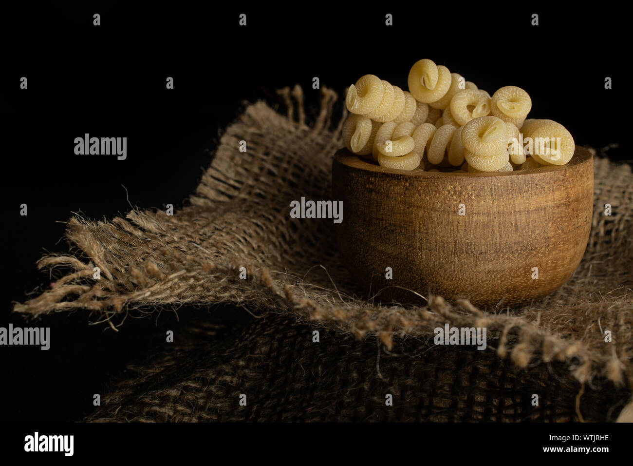 Beaucoup d'entiers et frais fusilli bucati pâtes crues dans bol en bois sur tissu du jute isolé sur verre noir Banque D'Images