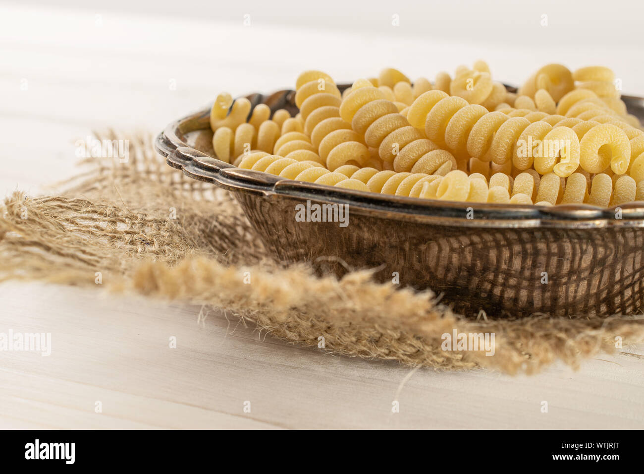Beaucoup d'entiers et frais fusilli bucati pâtes crues dans le vieux bol de fer sur le tissu du jute sur bois blanc Banque D'Images