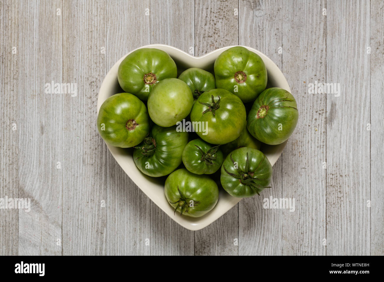 Les tomates vertes fraîches bio dans un bol en forme de coeur en bois blanc isolé sur une carte. Banque D'Images