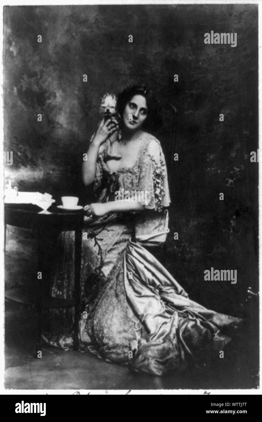 Mme Patrick Campbell, actrice, portrait en pied, assis à une petite table, en face légèrement à droite, holding pet dog Banque D'Images