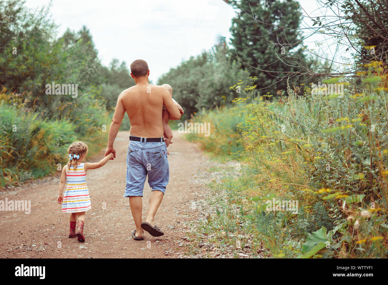 Le père marche avec les enfants sur une route de campagne tenant la main de  sa fille et de porter le bébé dans ses bras Photo Stock - Alamy
