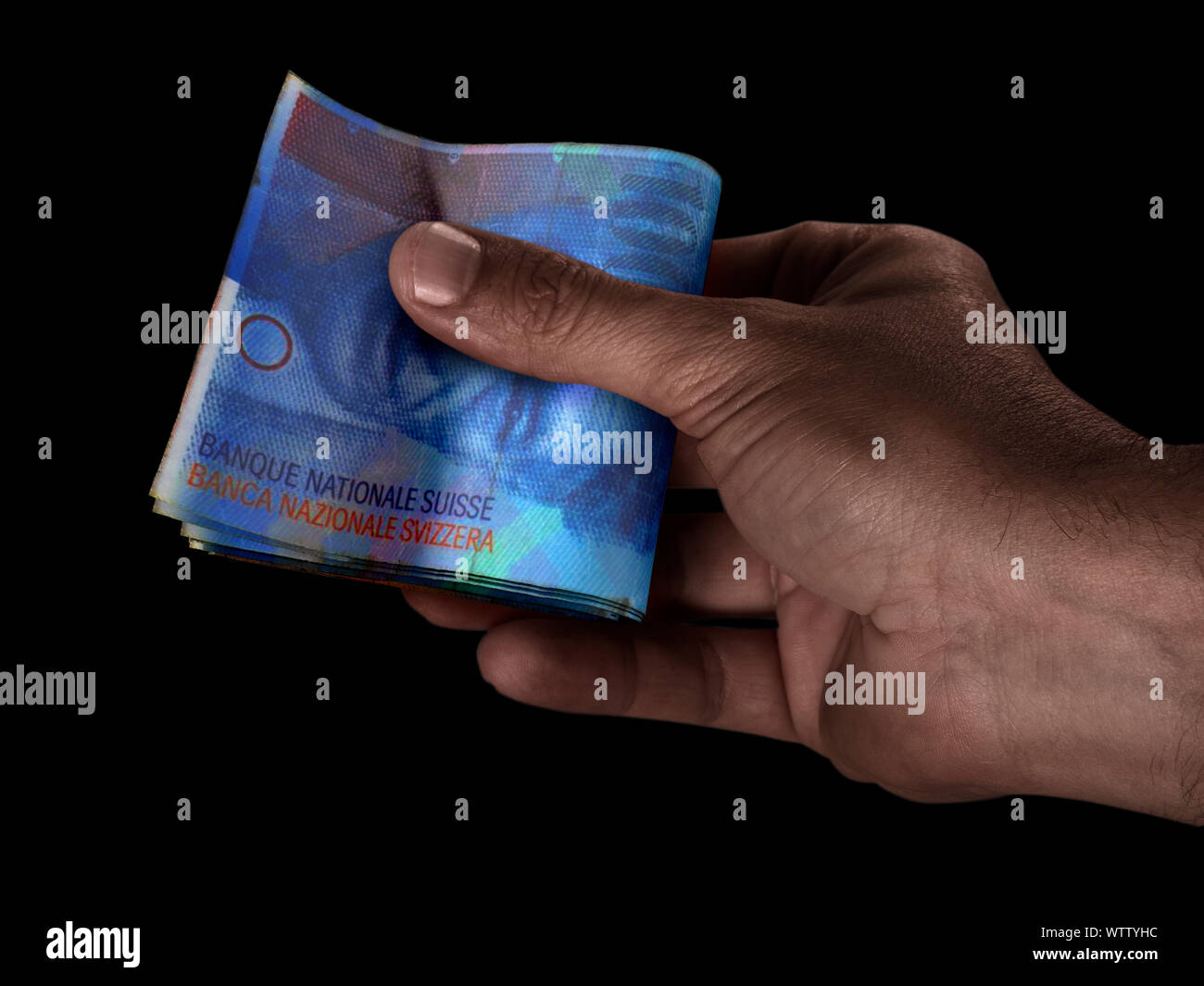 Un homme de race noire part remettre une liasse de billets de banque en francs pliés sur un fond isolé Banque D'Images
