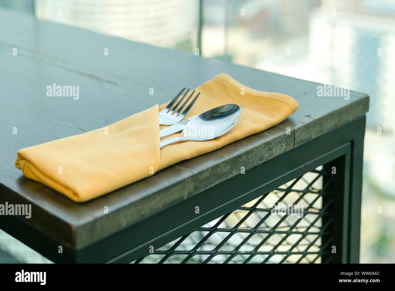 Cuillère, fourchette et couteau dans une couleur orange serviette sur une table en bois avec une vue sur piscine Banque D'Images