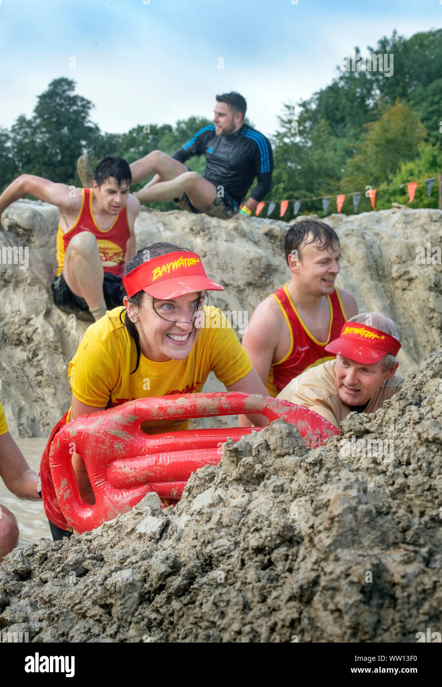 Une équipe de concurrents habillés comme des sauveteurs de Baywatch négocier la 'Mud kilomètre" à la dure épreuve d'endurance en Badminton Mudder Park, Gloucestershire U Banque D'Images