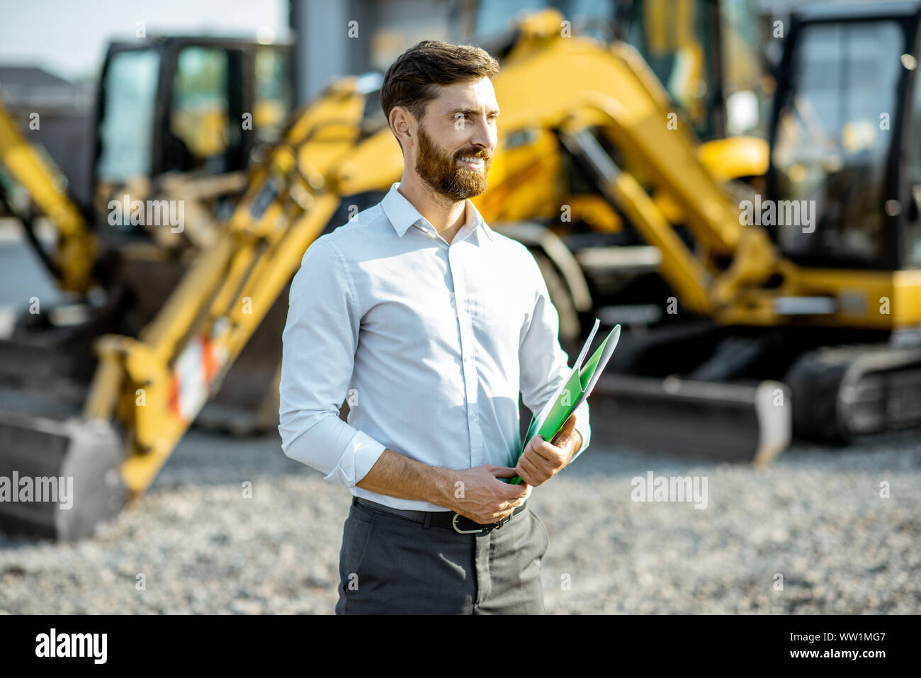 Portrait of a handsome sales consultant ou manager debout sur le terrain ouvert de la boutique avec des machines lourdes pour la construction Banque D'Images