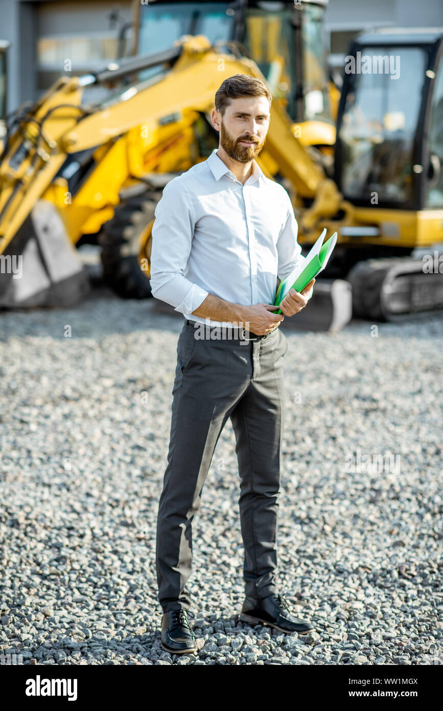 Portrait of a handsome sales consultant ou manager debout sur le terrain ouvert de la boutique avec des machines lourdes pour la construction Banque D'Images