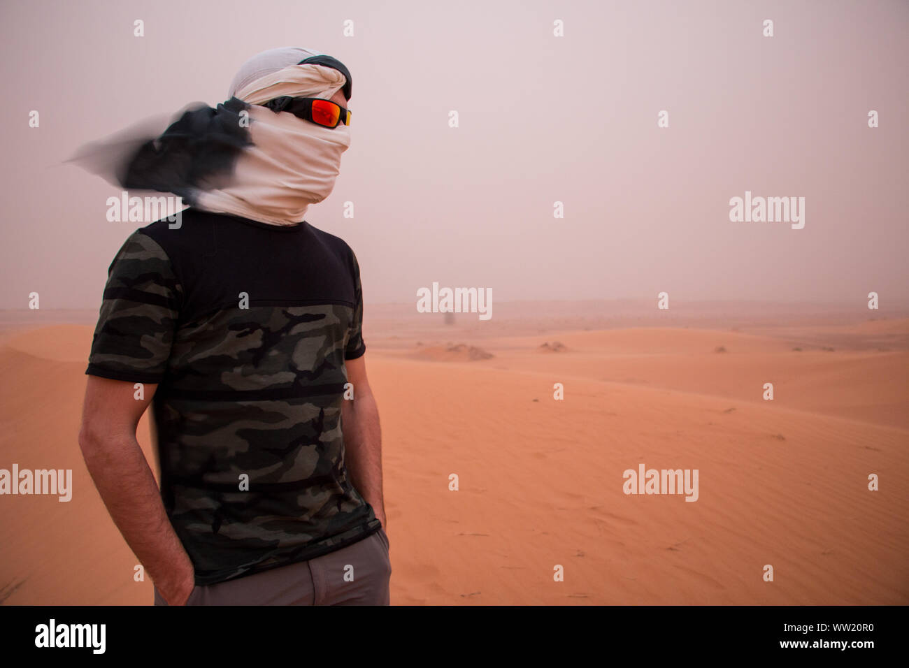 Un homme, la tête couverte par un foulard et des lunettes de soleil pendant une tempête de sable dans le désert Banque D'Images