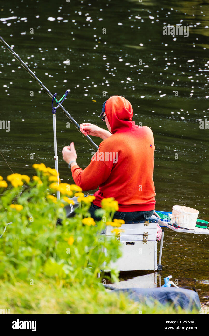 Un homme en veste rouge vif, pêche dans la rivière Trent, Gunthorpe, Nottinghamshire. Banque D'Images