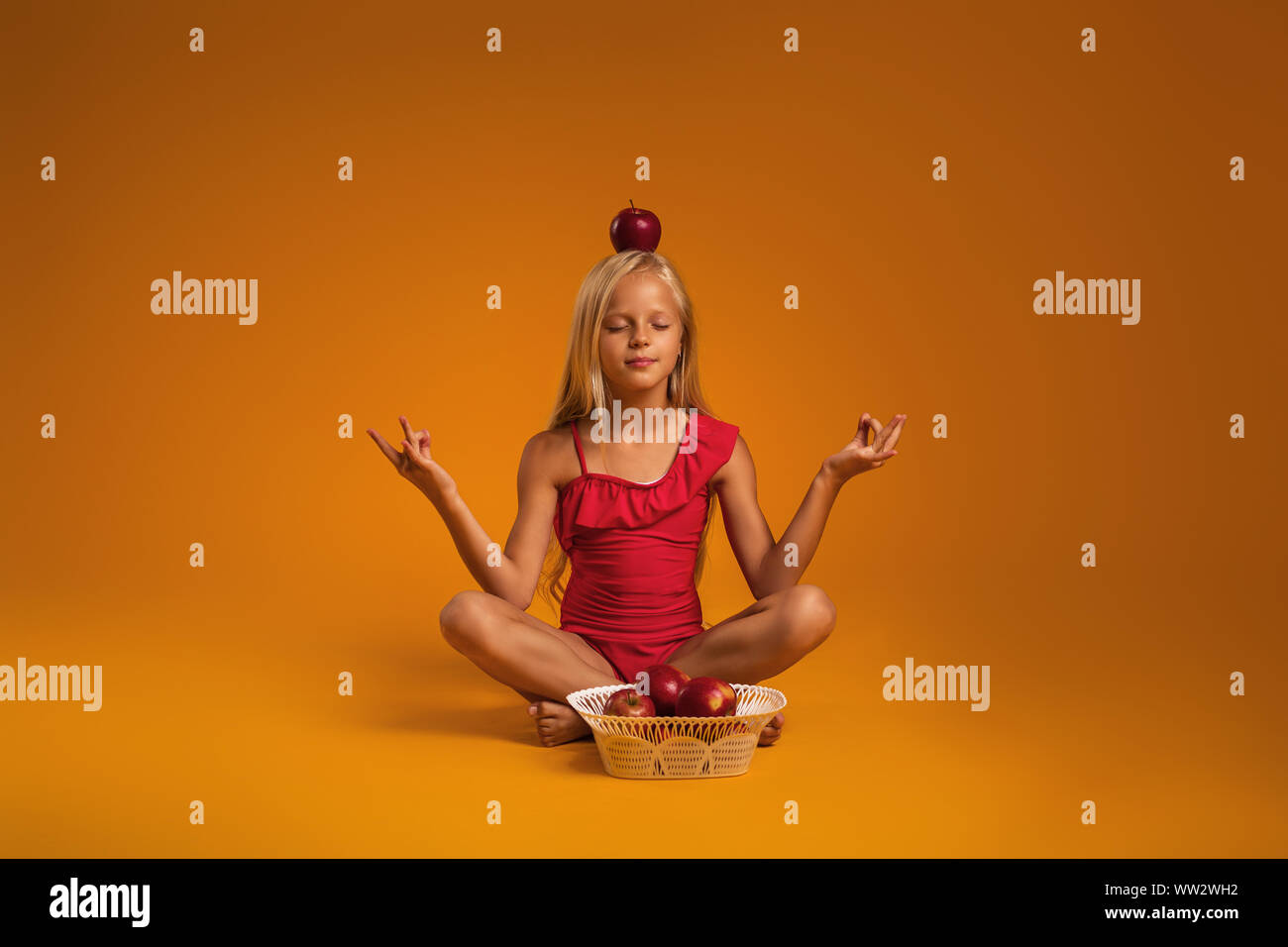 Petit enfant fille en maillot rouge assis en position du lotus sur fond orange. Banque D'Images