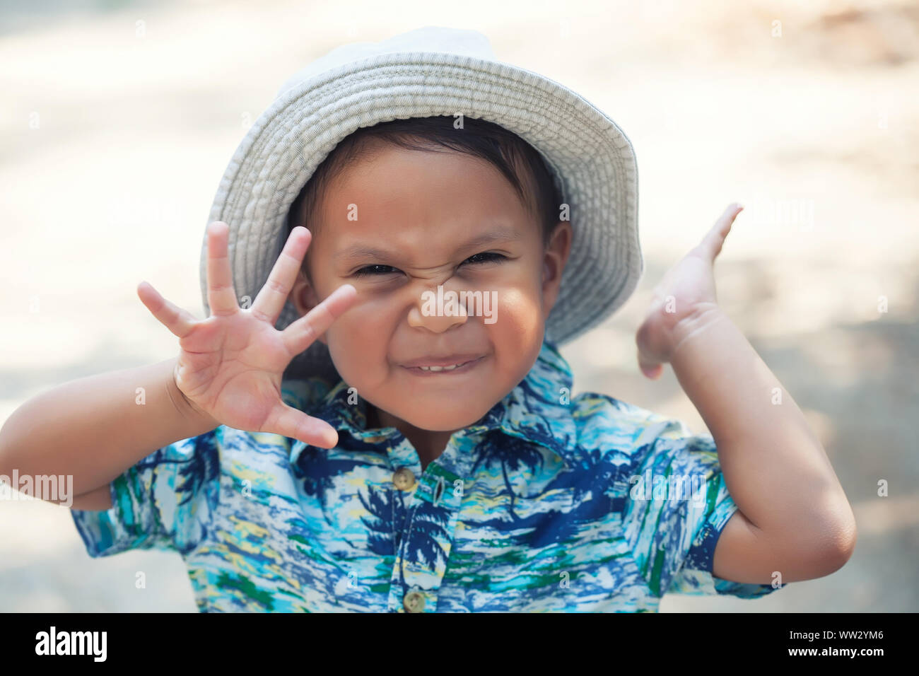 Un petit garçon énergique et heureux de faire une drôle de l'expression du visage et forme avec ses mains pour dire bonjour. Banque D'Images