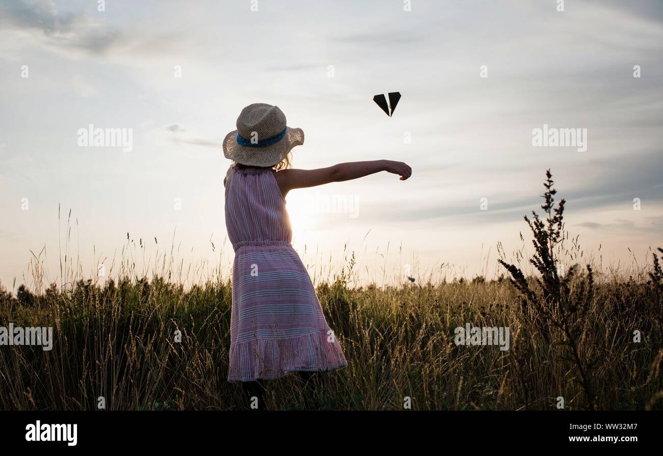 Jeune fille jouant avec un avion en papier dans un pré au coucher du soleil en été Banque D'Images