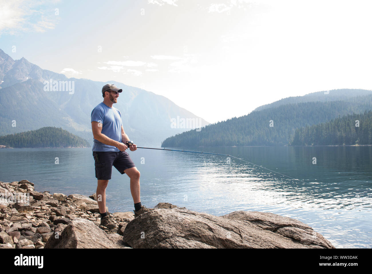 Homme debout sur les rochers de sourire et de la pêche à un lac à Washington Banque D'Images