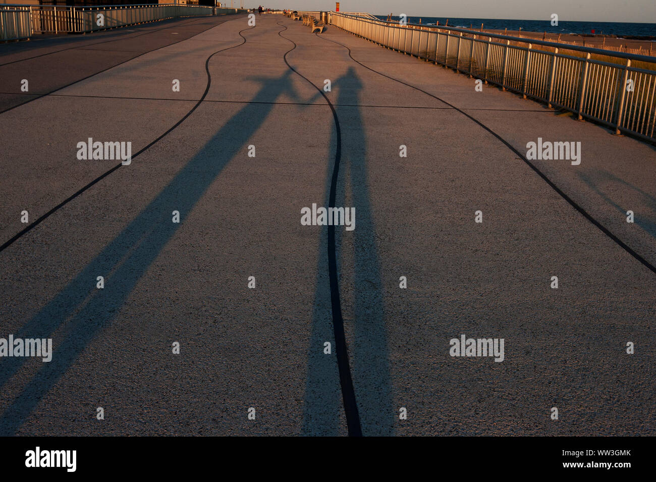 La lumière de la fin de l'après-midi projette de longues ombres sur les amis qui marchent sur la promenade Banque D'Images