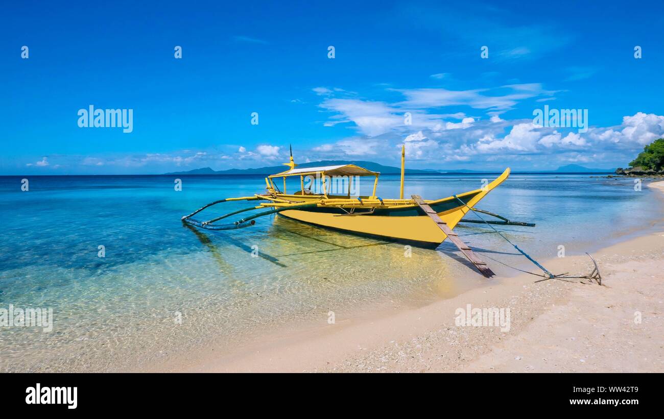 Une belle île tropicale avec une scène en bois traditionnels philippins bateau outrigger appelé banca, ancrée dans l'eau turquoise peu profonde claire sur un whi Banque D'Images