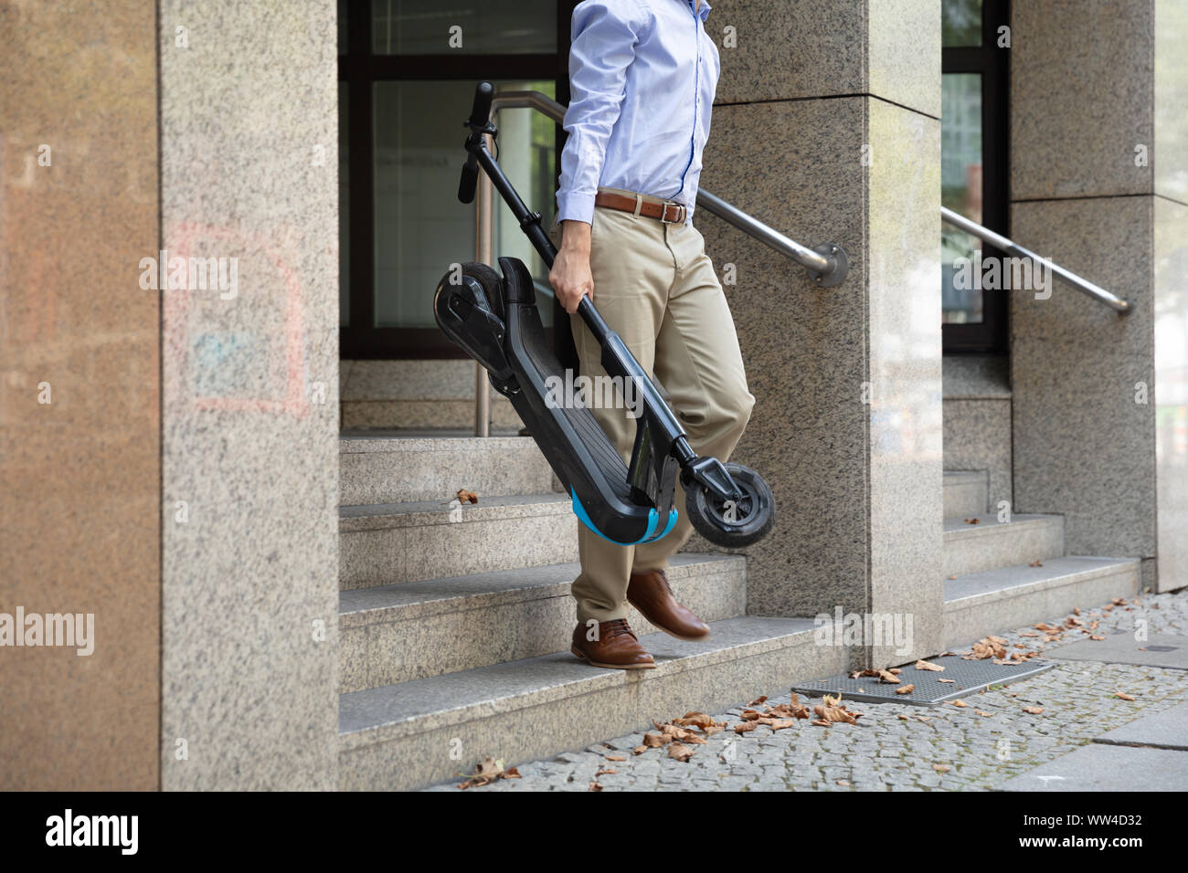 Homme portant l'E-scooter de travailler à la sortie de l'immeuble de bureaux Banque D'Images